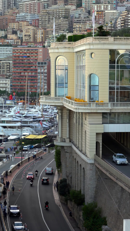 La Condamine, Monaco – July 8, 2025: Curving roadway leading to a yacht-packed marina, with the Belle-Epoque building and a dense hillside city beyond. Vertical - Starpik Stock