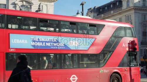 London, England – May 11, 2025: Busy day at Piccadilly Circus with crowds, Union Jack flags, historic buildings and a red double-decker bus driving - Starpik Stock