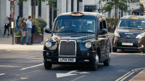 London, England – May 11, 2025: Classic black cab taxi driving through Regent street with pedestrians in the background - Starpik Stock