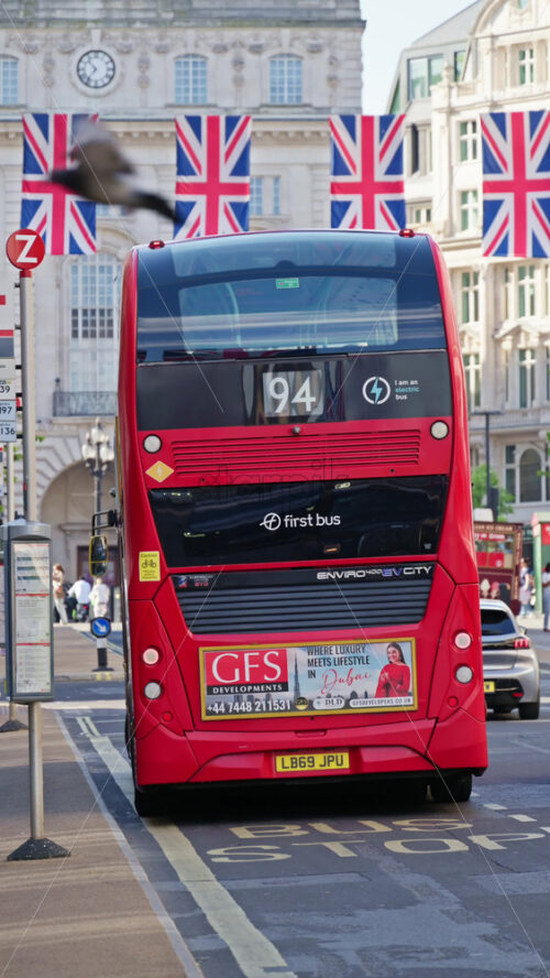 London, England – May 11, 2025: People getting on a red double-decker bus under Union Jack banners with Regent street in the background. Vertical - Starpik Stock