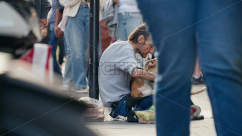 London, England – May 11, 2025: People walking by a homeless man sitting on the Piccadilly Circus sidewalk with a dog, water and food - Starpik Stock