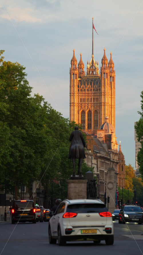 London, England – May 11, 2025: Street view in Westminster with cars passing a bronze statue and historic tower in the background at sunset. Vertical - Starpik Stock
