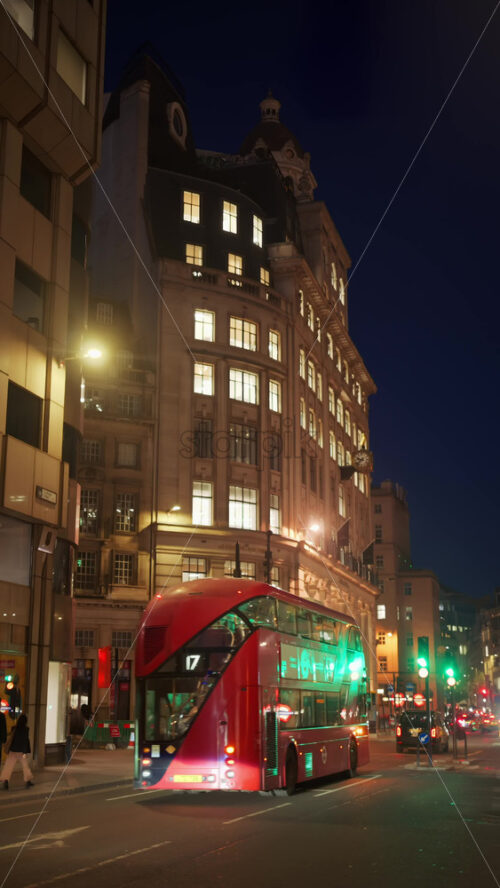 London, England – May 12, 2025: Busy street with red buses, pedestrians and traditional city buildings in the evening. Vertical - Starpik Stock