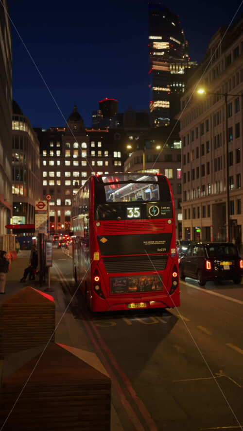 London, England – May 12, 2025: Busy street with red buses, pedestrians and traditional city buildings in the evening. Vertical - Starpik Stock