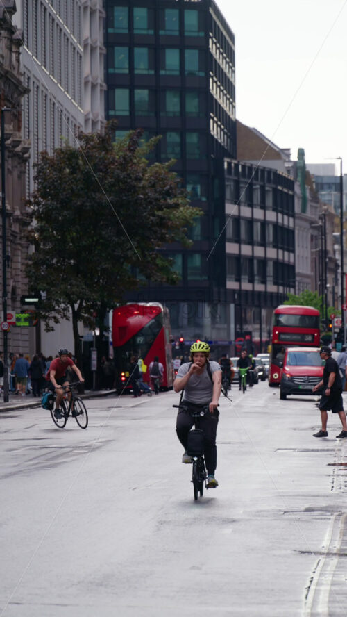 London, England – May 12, 2025: Busy street with red buses, pedestrians at a bus stop, and traditional city buildings. Vertical - Starpik Stock