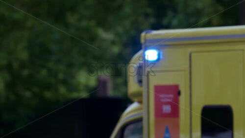 London, England – May 12, 2025: Close up of an ambulance with flashing lights driving through a busy intersection surrounded by pedestrians and vehicles - Starpik Stock