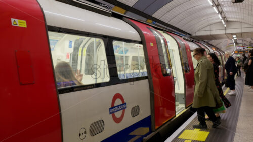 London, England – May 12, 2025: Commuters boarding a red and white Underground train inside a modern tube station during the evening rush hour - Starpik Stock