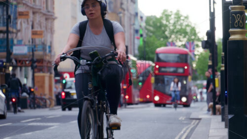 London, England – May 12, 2025: Cyclists and classic red double-decker buses, with Union Jack flags lining the road in the evening - Starpik Stock