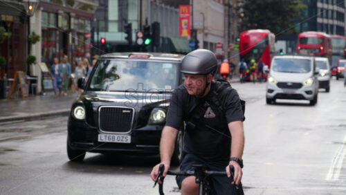 London, England – May 12, 2025: Group of cyclists navigating through the city center traffic alongside pedestrians and red double-decker buses - Starpik Stock