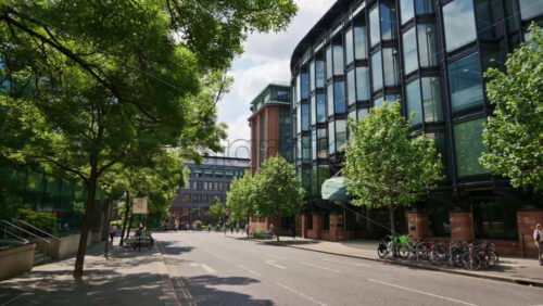 London, England – May 12, 2025: Modern business district in the city center with tree-lined street, bicycles, and glass buildings in daylight - Starpik Stock