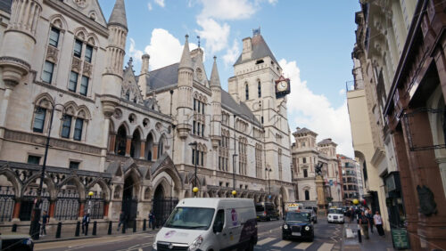 London, England – May 12, 2025: The clock tower and street view of the Royal Courts of Justice with vehicles and pedestrians passing by - Starpik Stock