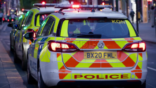 London, England – May 12, 2025: UK police cars with flashing blue lights parked on a busy street, passing pedestrians and cyclists during the day - Starpik Stock
