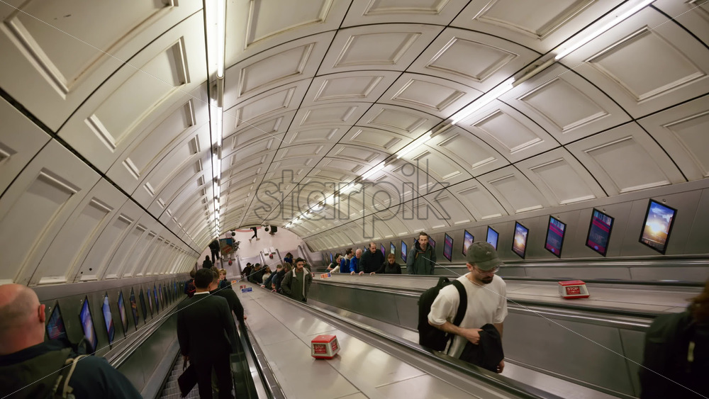 London, England – May 12, 2025: View of a deep London Underground escalator tunnel with people ascending and descending in the evening - Starpik Stock