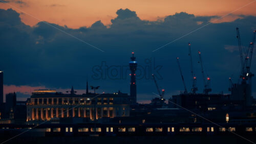 London, England – May 12, 2025: View of the city skyline at dusk featuring the BT Tower and construction cranes under a purple and blue sky - Starpik Stock