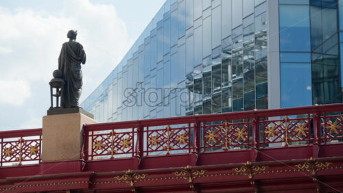 London, England – May 12, 2025: Woman statue on a red bridge Holborn viaduct with a woman walking on it in the financial district. - Starpik Stock