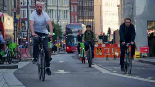 London, England – May 13, 2025: A group of cyclists commuting through the city on a sunny morning with glass buildings in the background - Starpik Stock