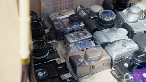 London, England – May 13, 2025: Assortment of vintage film and digital point and shoot cameras laid out on a vendor’s table at Spitalfields Market, featuring brands like Canon and Olympus - Starpik Stock