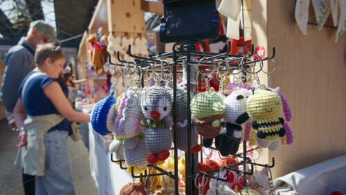 London, England – May 13, 2025: Close up of colourful crochet keychains hanging on display at Spitalfields Market, with people browsing stalls in the background - Starpik Stock