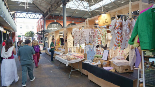 London, England – May 13, 2025: Shoppers walking through a covered section of Spitalfields Market, passing stalls selling clothes, artwork, and handmade items - Starpik Stock