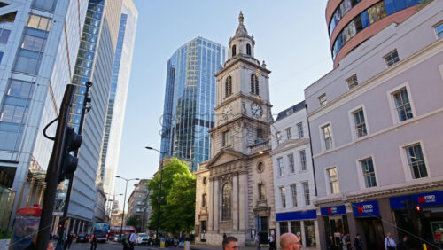 London, England – May 13, 2025: St. Botolph-without-Bishopsgate church standing prominently at the edge of Liverpool Street, framed by gleaming glass towers with pedestrians passing on the street - Starpik Stock