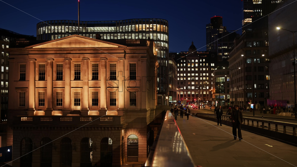 London, England – May 13, 2025: The Fishmongers Hall building lit up at dusk, surrounded by modern high-rise buildings in the city center - Starpik Stock