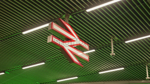 London, England – May 13, 2025: The iconic National Rail symbol under fluorescent lighting and security cameras overhead. - Starpik Stock