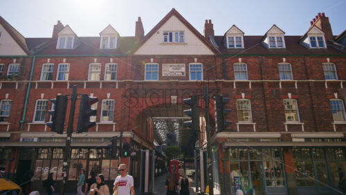 London, England – May 13, 2025: View of the iconic red-brick Spitalfields Market entrance with pedestrians walking around - Starpik Stock