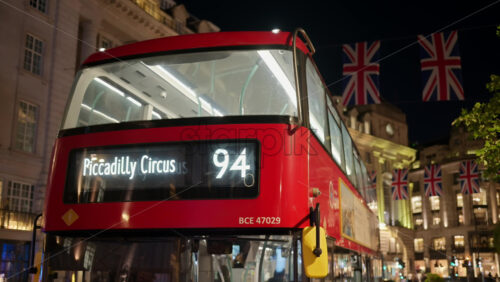 London, England – May 14, 2025: A red double-decker bus to Piccadilly Circus glides through Regent Street with UK flags - Starpik Stock