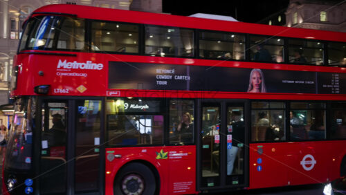 London, England – May 14, 2025: A red double-decker bus traveling down a brightly lit Piccadilly Circus decorated with UK flags in the evening - Starpik Stock