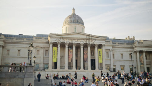 London, England – May 14, 2025: People sitting and moving on the steps of the The National Gallery museum in daylight. Trafalgar Square - Starpik Stock