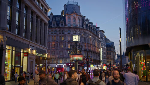 London, England – May 14, 2025: People walking through Leicester square in the evening, with Swiss Glockenspiel and historic buildings in view - Starpik Stock