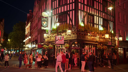 London, England – May 14, 2025: The Three Greyhounds pub glows at night as people gather outside in a festive atmosphere of Soho - Starpik Stock