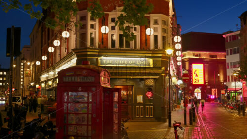 London, England – May 14, 2025: Time lapse of a warmly lit view of people moving near The Spice of Life pub next to a red phone booth in the evening. Soho - Starpik Stock