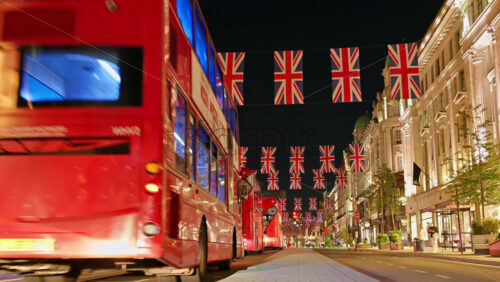 London, England – May 14, 2025: Time lapse of cars and public transportation driving through Regent street decorated with multiple Union Jack flags at night - Starpik Stock