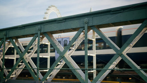 London, England – May 14, 2025: Train crossing a metal bridge with the London Eye in the background - Starpik Stock