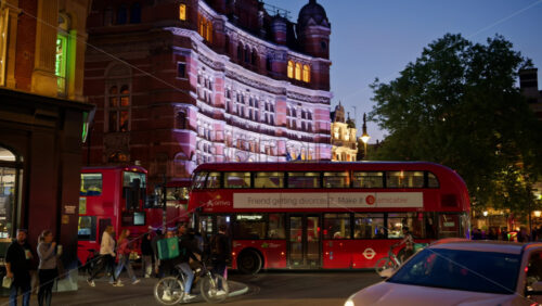 London, England – May 14, 2025: Two red buses driving past the Shaftesbury Theatre under golden evening lights of Soho - Starpik Stock