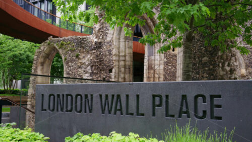 London, England – May 15, 2025: Close-up of a stone sign reading London Wall Place with ancient stone ruins and green trees in the background, blending history with urban nature - Starpik Stock