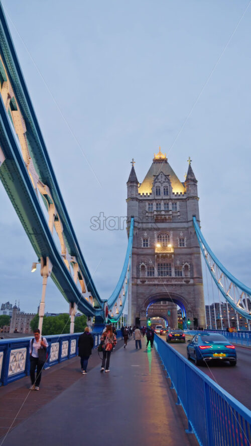 London, England – May 15, 2025: Close up of the Tower Bridge at twilight with blue lighting on the arches and people walking on it. Vertical - Starpik Stock