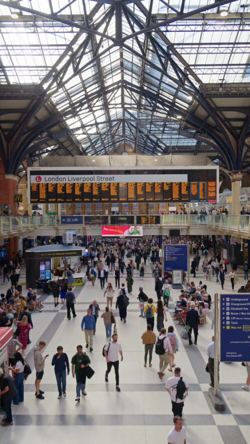 London, England – May 15, 2025: Interior of Liverpool Street busy train station with a high glass ceiling and brick walls filled with commuters. Vertical - Starpik Stock