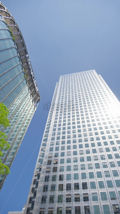 London, England – May 15, 2025: Low angle view of One Canada Square Canary Wharf modern glass office buildings with sunlight reflecting on them. Vertical - Starpik Stock