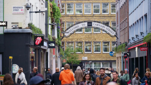 London, England – May 15, 2025: People walking under Carnaby Street sign with many store signs - Starpik Stock