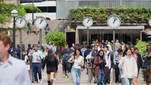 London, England – May 16, 2025: Busy pedestrian street filled with people walking, flanked by modern clocks on poles - Starpik Stock