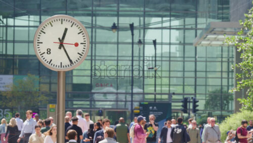London, England – May 16, 2025: Busy pedestrian street filled with people walking, flanked by modern clocks on poles. Canary Wharf - Starpik Stock