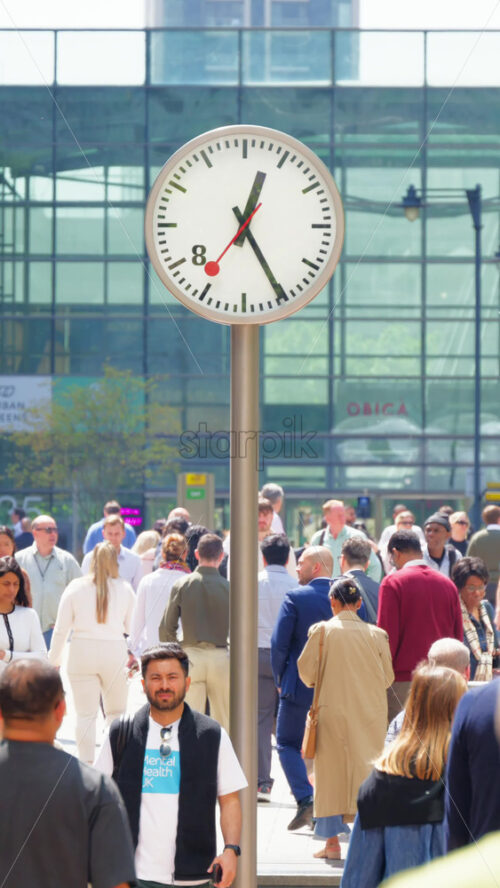 London, England – May 16, 2025: Busy pedestrian street filled with people walking, flanked by modern clocks on poles. Vertical - Starpik Stock