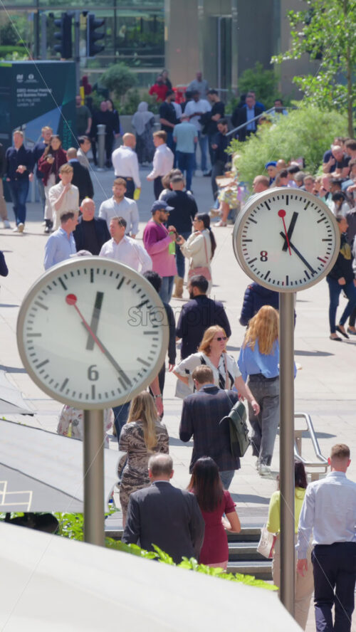 London, England – May 16, 2025: Busy pedestrian street filled with people walking, flanked by modern clocks on poles. Vertical - Starpik Stock