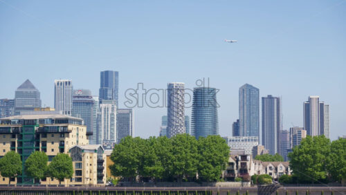 London, England – May 16, 2025: Close up of greenery with the Canary Wharf skyline in the background in daylight. Airplane passing by - Starpik Stock