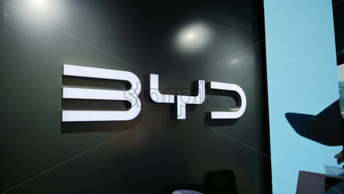 London, England – May 16, 2025: Illuminated BYD company logo mounted on a dark wall, with reflections from digital displays nearby - Starpik Stock