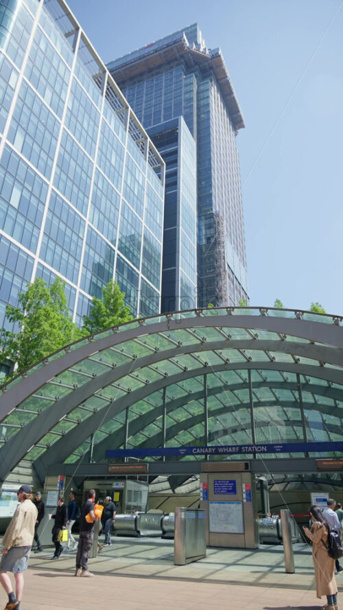 London, England – May 16, 2025: Modern architectural view of Canary Wharf Station entrance featuring a glass and steel canopy with office towers in the background. Vertical - Starpik Stock