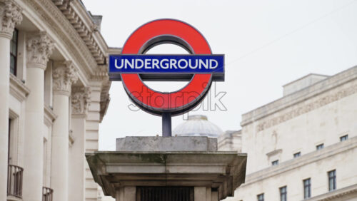 London Underground entrance sign in daylight, framed by neoclassical architecture and urban background - Starpik Stock