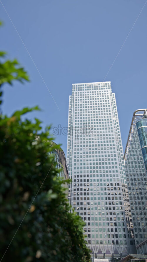 Low angle view of One Canada Square modern glass office buildings with sunlight reflecting on them in Canary Wharf, London, England. Vertical - Starpik Stock